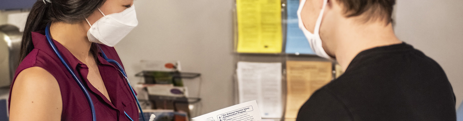 A doctor in a mask shows a piece of paper with medical information on it to a patient also in a mask.