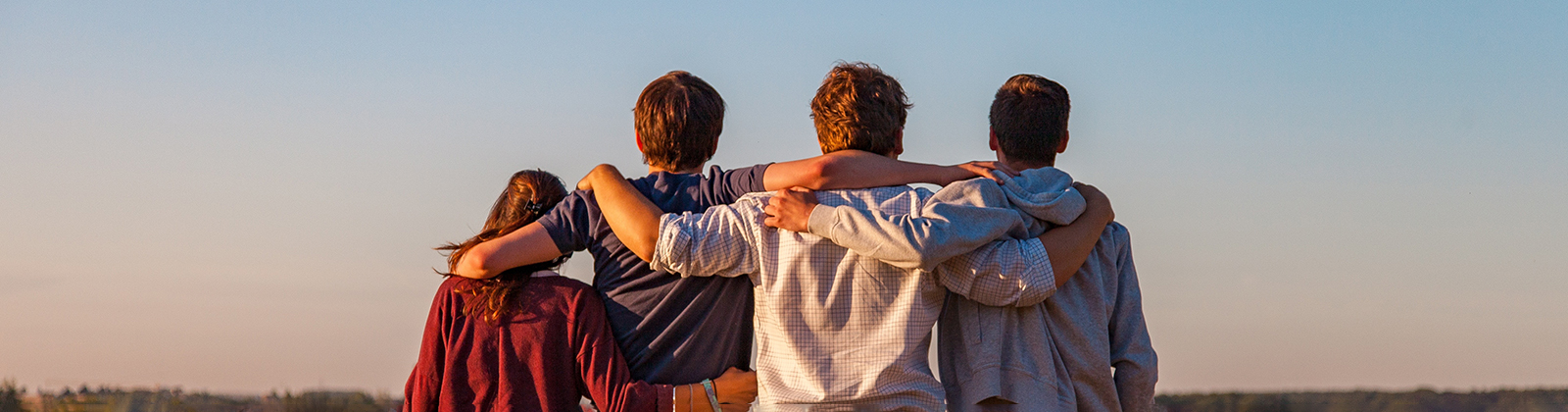 A group of people stand facing away from the camera with their arms around each other's shoulders.